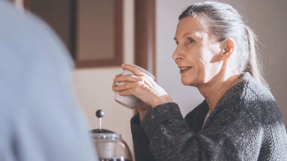 An older woman holding a mug in conversation over coffee