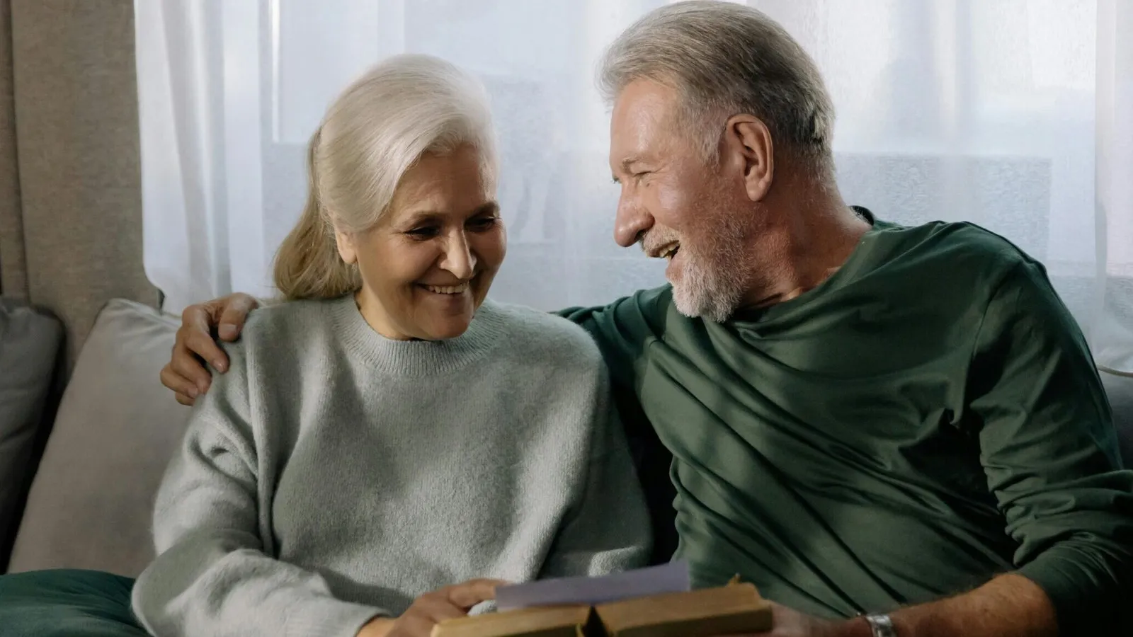 An older couple sitting together on a sofa with a book